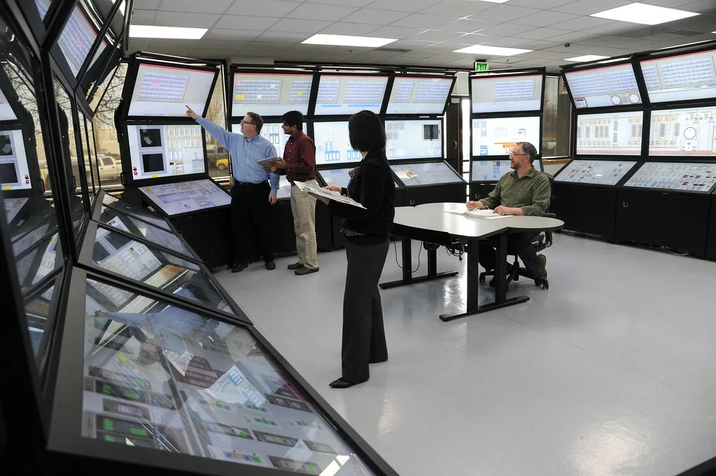 Operators at a control room desk in front of a wall of screens