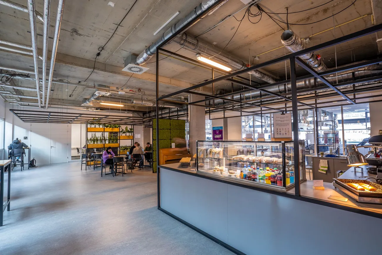Large staff canteen with exposed ducting, a glass food counter and employees eating at tables
