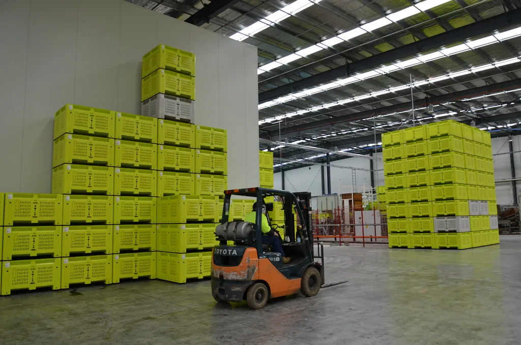 Counterbalance forklift moving stacked crates inside a packing warehouse